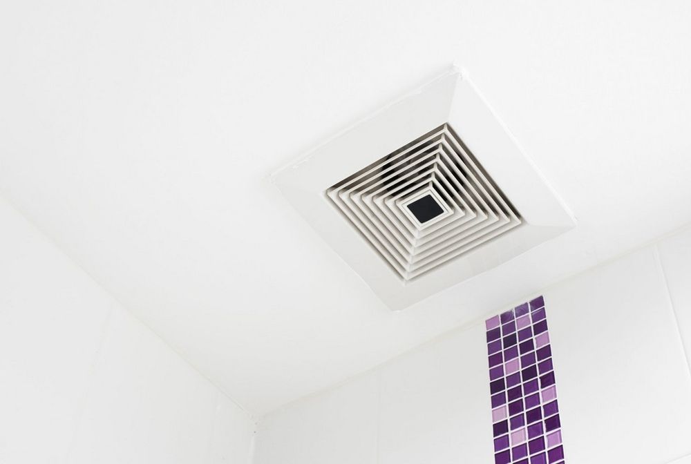 Deckenlüftungsgitter mit quadratischem Muster an weißer Decke und lila Mosaikfliesen an der Wand